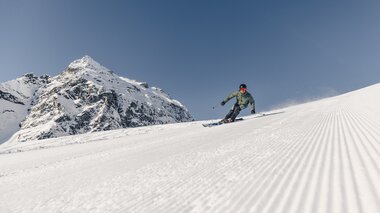 Skifahrer in grüner Jacke fährt schwungvoll eine frisch präparierte Piste in Gargellen hinunter, Berggipfel im Hintergrund. | © Gargellner Bergbahnen, Daniel Zangerl
