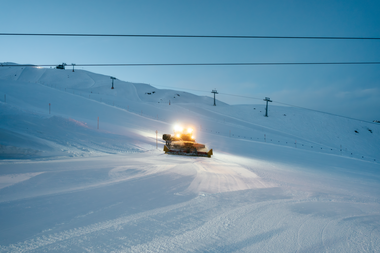 Eine Pistenraupe bereitet in der Abenddämmerung die Skipisten von Gargellen im Montafon vor. Die Scheinwerfer leuchten über die frisch präparierte Schneefläche, im Hintergrund sind die Skilifte und verschneiten Hänge zu sehen. | © Montafon Tourismus GmbH, Marie Schilcher