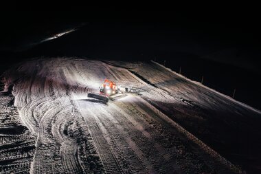 Eine Pistenraupe präpariert in der Nacht die verschneiten Hänge von Gargellen im Montafon. Die Scheinwerfer leuchten die Piste aus und erzeugen ein beeindruckendes Lichtspiel auf dem frisch bearbeiteten Schnee. | © Montafon Tourismus GmbH, Marie Schilcher