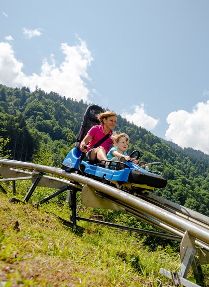 Eine Frau und ein Kind fahren auf einer Sommerrodelbahn den Berg hinunter | © Golm Silvretta Lünersee Tourismus GmbH Bregenz, Stefan Kothner