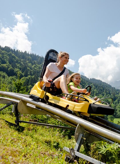 Eine Frau und ein Kind fahren auf einer Sommerrodelbahn den Berg hinunter | © Golm Silvretta Lünersee Tourismus GmbH Bregenz, Stefan Kothner