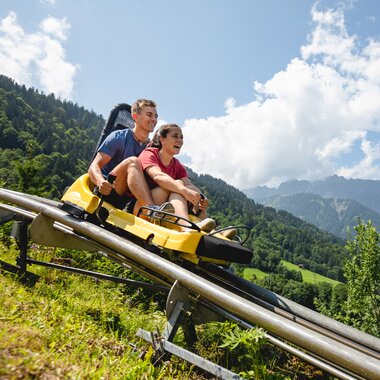 Eine Frau und ein Mann fahren auf einer Sommerrodelbahn den Berg hinunter | © Golm Silvretta Lünersee Tourismus GmbH Bregenz, Stefan Kothner