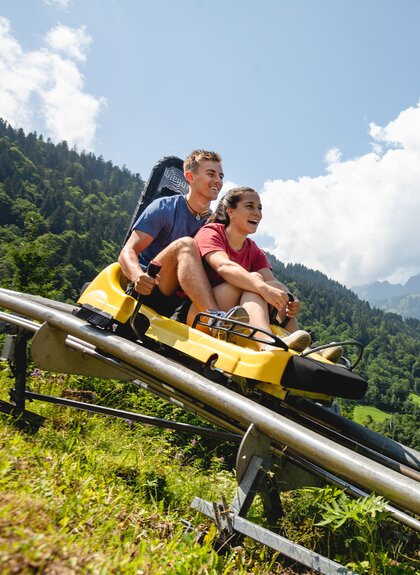 Eine Frau und ein Mann fahren auf einer Sommerrodelbahn den Berg hinunter | © Golm Silvretta Lünersee Tourismus GmbH Bregenz, Stefan Kothner