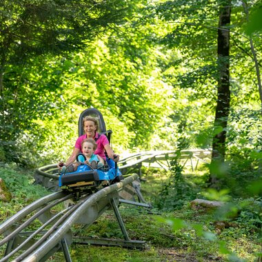 Eine Frau und ein Kind fahren auf einer Sommerrodelbahn durch den Wald hinunter | © Golm Silvretta Lünersee Tourismus GmbH Bregenz, Stefan Kothner