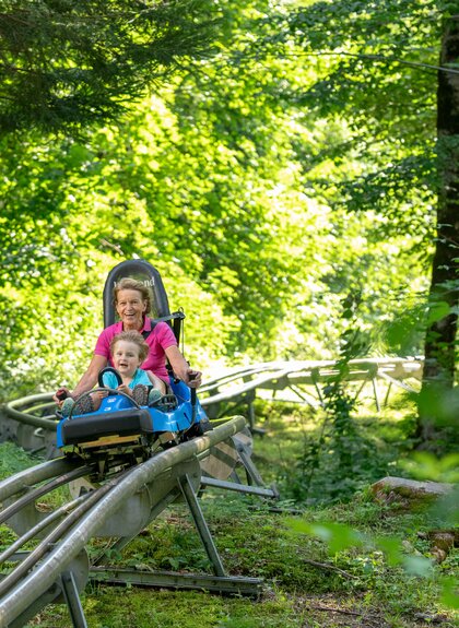 Eine Frau und ein Kind fahren auf einer Sommerrodelbahn durch den Wald hinunter | © Golm Silvretta Lünersee Tourismus GmbH Bregenz, Stefan Kothner