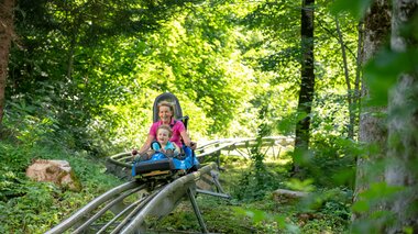 A woman and a child ride down through a forest on a summer roller coaster | © Golm Silvretta Lünersee Tourismus GmbH Bregenz, Stefan Kothner
