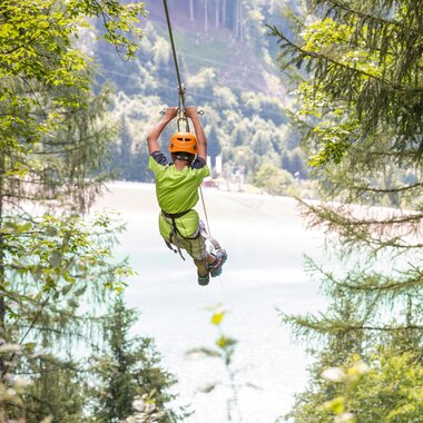 Ein Mädchen das mit einem 565 m langen Stahlseil befestigt über das Staubecken Latschau fliegt | © Golm Silvretta Lünersee Tourismus GmbH Bregenz, Stefan Kothner