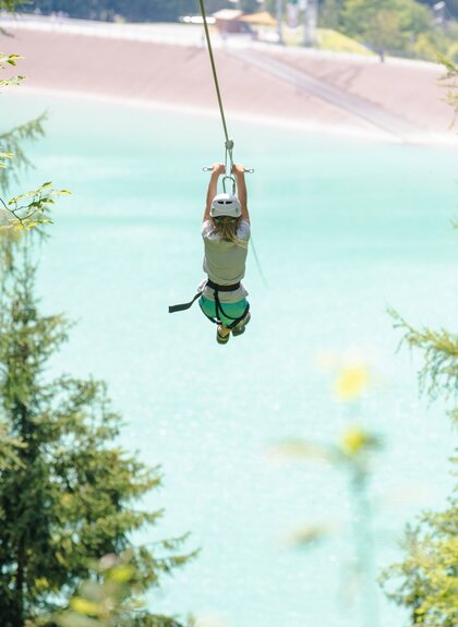A man flying over the Latschau reservoir attached to a 565 m long steel cable | © Golm Silvretta Lünersee Tourismus GmbH Bregenz, Stefan Kothner