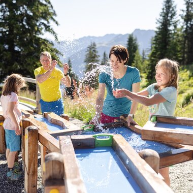 Vater und Mutter, die gemeinsam mit ihren zwei Töchtern beim Wasserspiel auf Golmis Forschungspfad die Kraft des Wassers entdecken | © Golm Silvretta Lünersee Tourismus GmbH Bregenz, Stefan Kothner