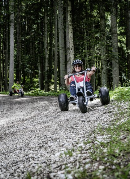 Freunde die mit Mountaincarts den Berg hinunter auf einer Schotterstraße hinunter fahren | © Mountaincart GmbH