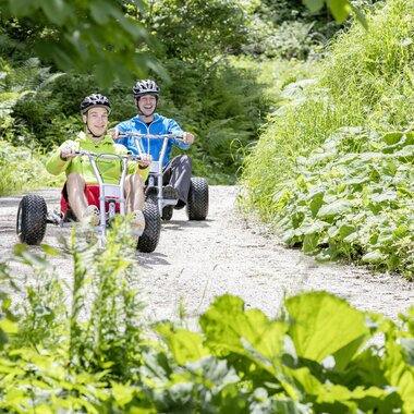Freunde die mit Mountaincarts den Berg hinunter auf einer Schotterstraße hinunter fahren | © Mountaincart GmbH