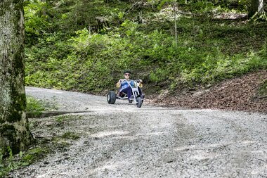 Frau die mit einem Mountaincart den Berg hinunter auf einer Schotterstraße fährt | © Mountaincart GmbH