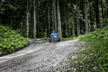 Mann der mit einem Mountaincart den Berg hinunter auf einer Schotterstraße fährt | © Mountaincart GmbH