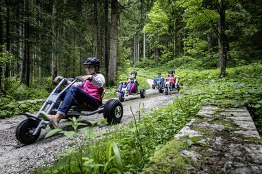 Freunde die mit Mountaincarts den Berg hinunter auf einer Schotterstraße hinunter fahren | © Mountaincart GmbH