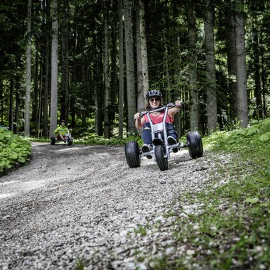 Freunde die mit Mountaincarts den Berg hinunter auf einer Schotterstraße hinunter fahren | © Mountaincart GmbH