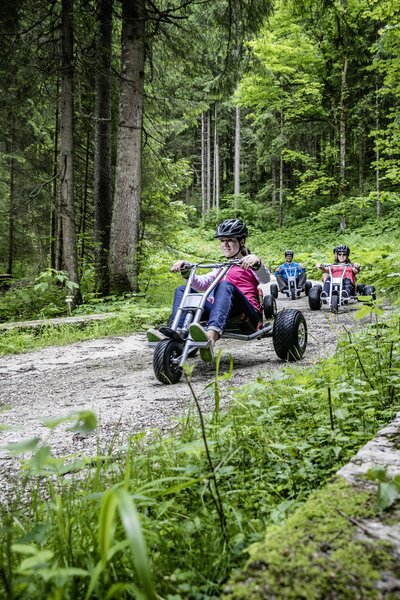 Freunde die mit Mountaincarts den Berg hinunter auf einer Schotterstraße hinunter fahren | © Mountaincart GmbH