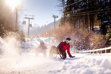 Zwei Freundinnen, die gerade die Rodelbahn am Erlebnisberg Golm hinunterrodeln und der Schnee stäubt auf | © Golm Silvretta Lünersee Tourismus GmbH Bregenz, Stefan Kothner