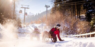 Zwei Freundinnen, die gerade die Rodelbahn am Erlebnisberg Golm hinunterrodeln und der Schnee stäubt auf | © Golm Silvretta Lünersee Tourismus GmbH Bregenz, Stefan Kothner