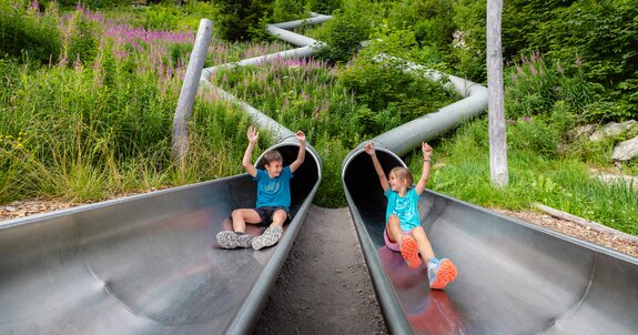 Zwei Kinder die gerade aus zwei einzelnen Rutschen am Waldrutschenpark-Golm rutschen | © Golm Silvretta Lünersee Tourismus GmbH Bregenz, Mathäus Gartner