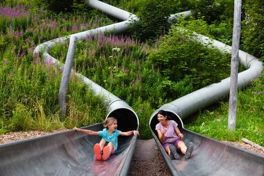 Waldrutschenpark-Golm im Montafon | © Golm Silvretta Lünersee Tourismus GmbH Bregenz, Stefan Kothner Mama mit Kind die zwei unterschiedliche Rutschen im Waldrutschenpark-Golm hinunterutschen | © Golm Silvretta Lünersee Tourismus GmbH Bregenz, Stefan Kothner
